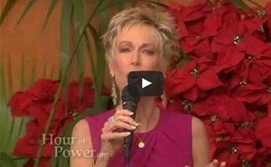 A woman in a pink dress is holding a microphone in front of red flowers.