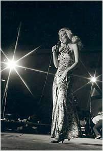 Singer performing on stage in a patterned gown under bright spotlights.