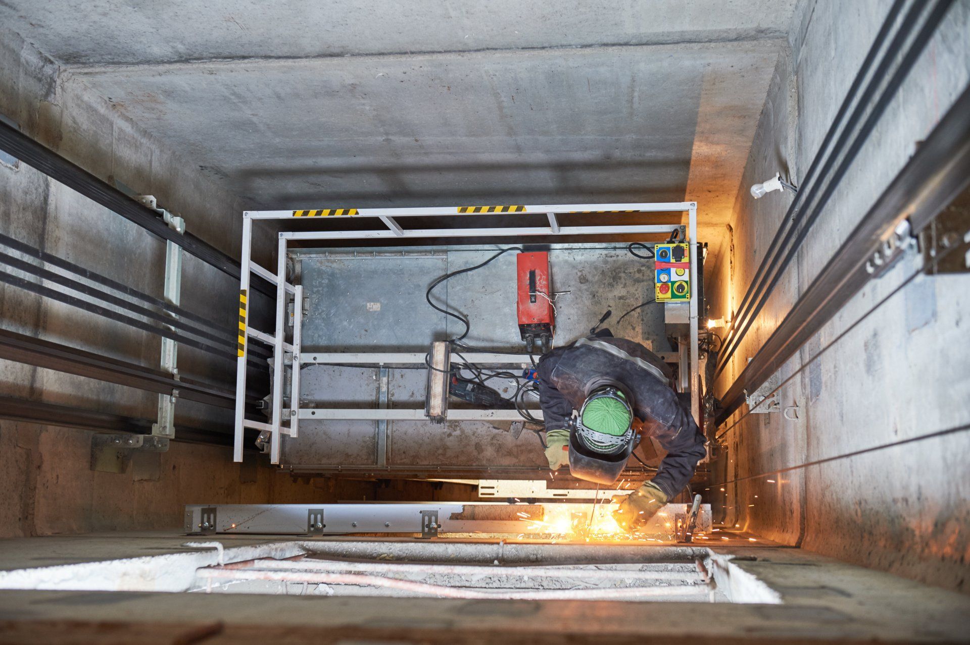 Elevator technician welding metal in a shaft, sparks flying.