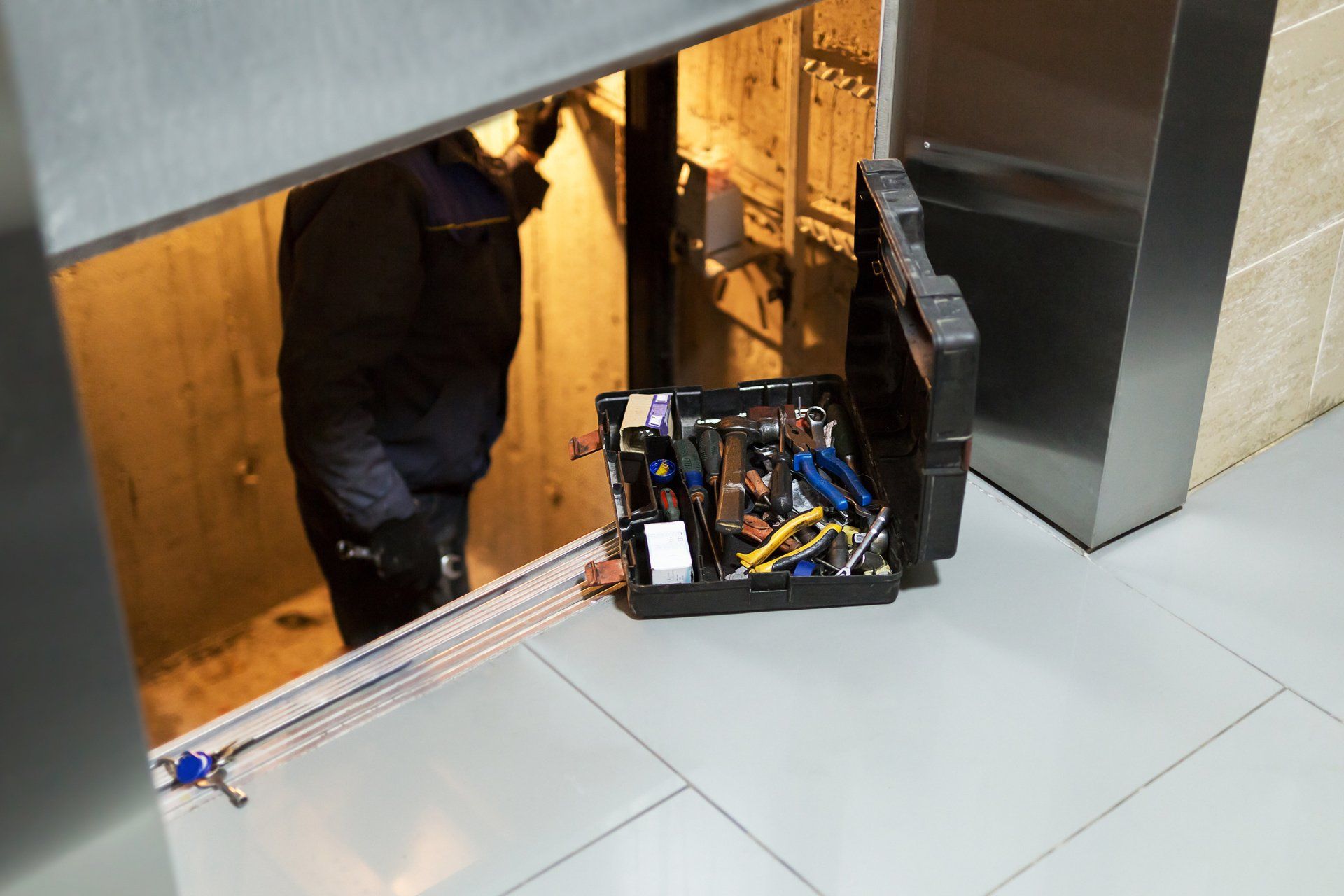 A toolbox with tools sits on the floor near an open doorway. A person in dark clothing is visible in the doorway.