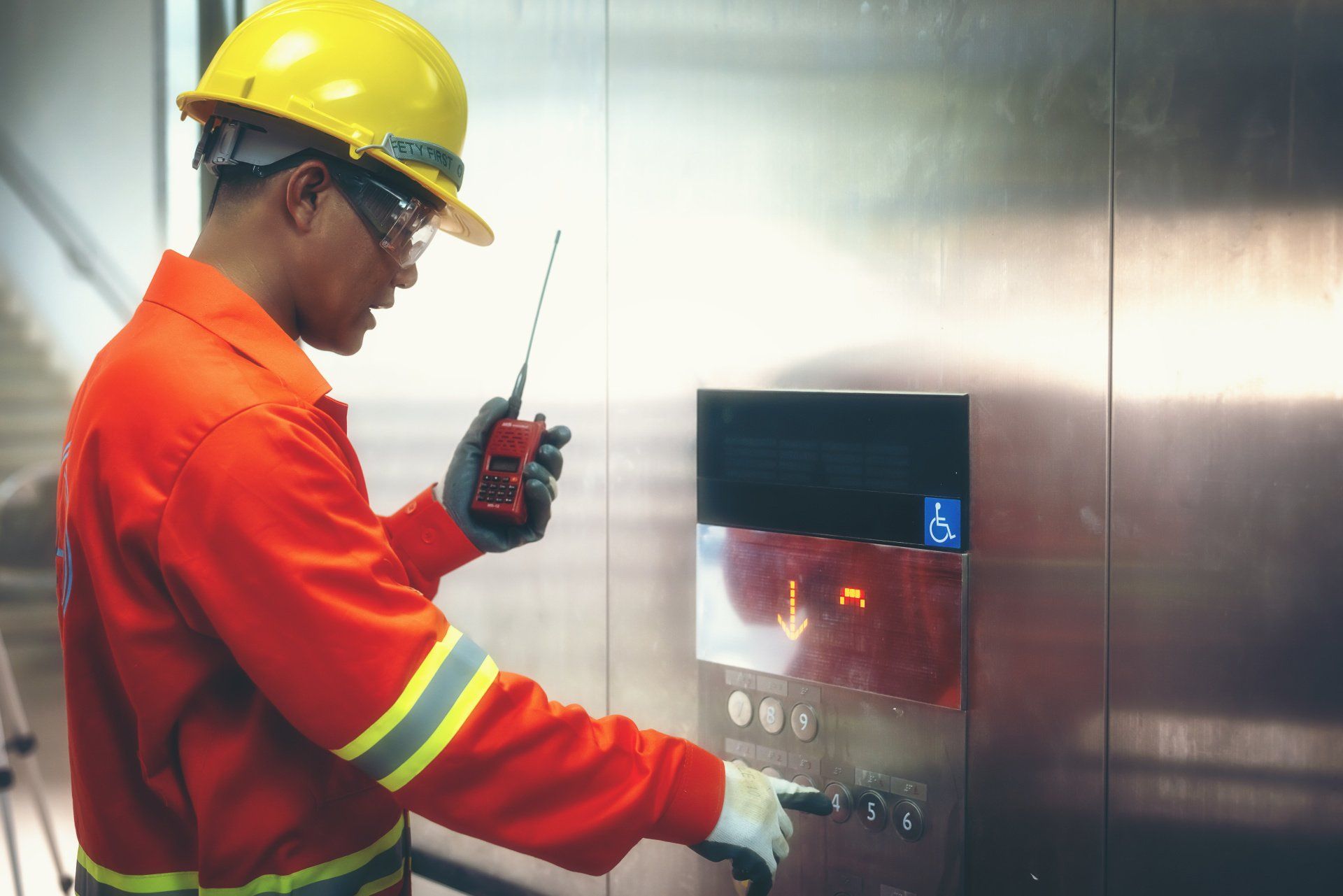 Man in safety gear operates elevator buttons, holding a radio.