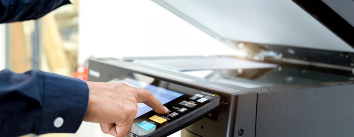 Person's hand pressing a button on a photocopier control panel.
