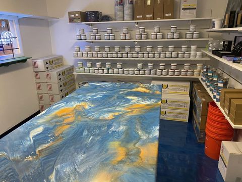 A room with a table and shelves filled with bottles of paint.