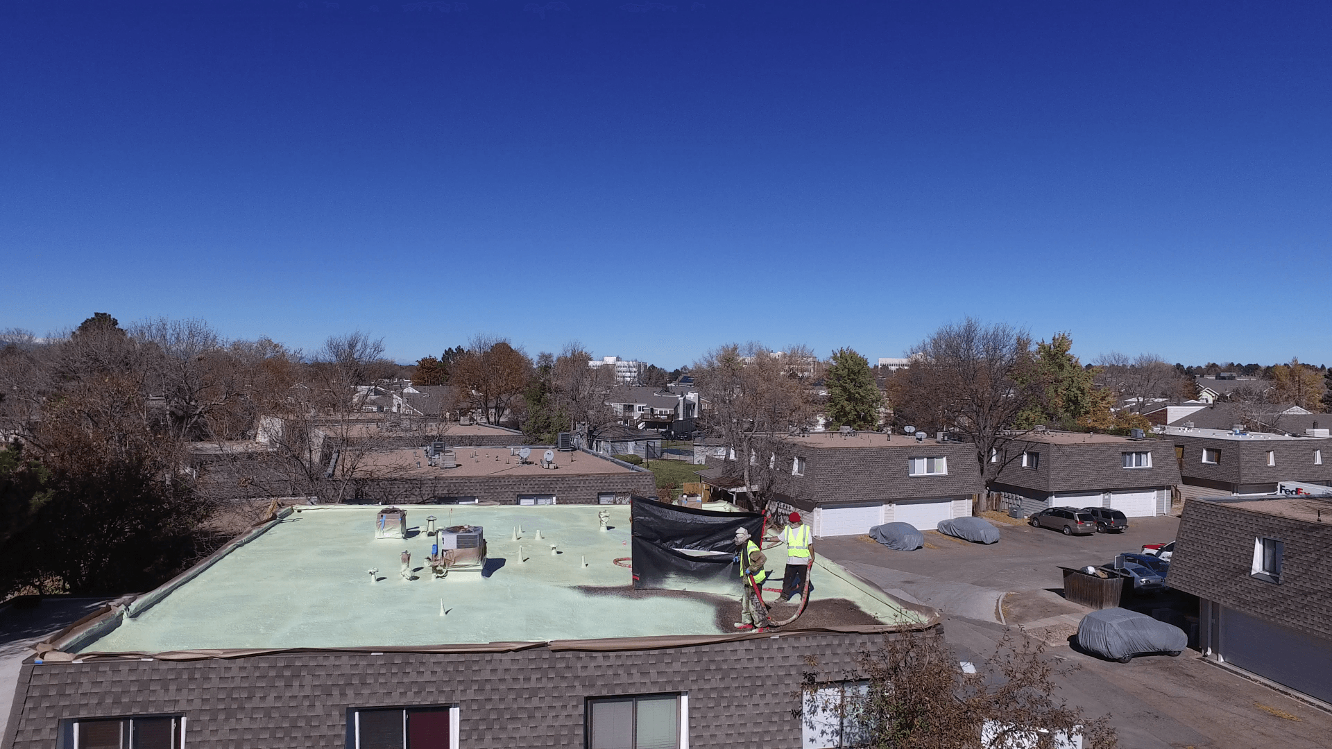 The roofing workers are in the last corner of the building applying a new coating to the roof.