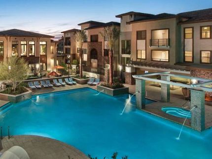 Nighttime view of a large lighted pool surrounded by multi-level housing units in an apartment complex