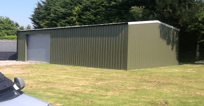Green corrugated metal shed with a large garage door, in a grassy yard.