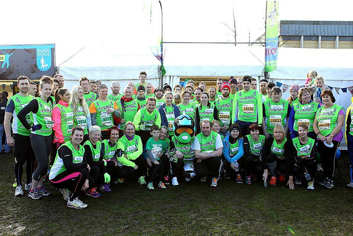 Group of people in green shirts pose in front of a tent, likely at a running event.