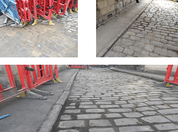 Cobblestone street with construction barriers; gray stones, red barriers.