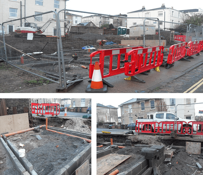 Construction site with red barriers, orange cones, and exposed pipes.
