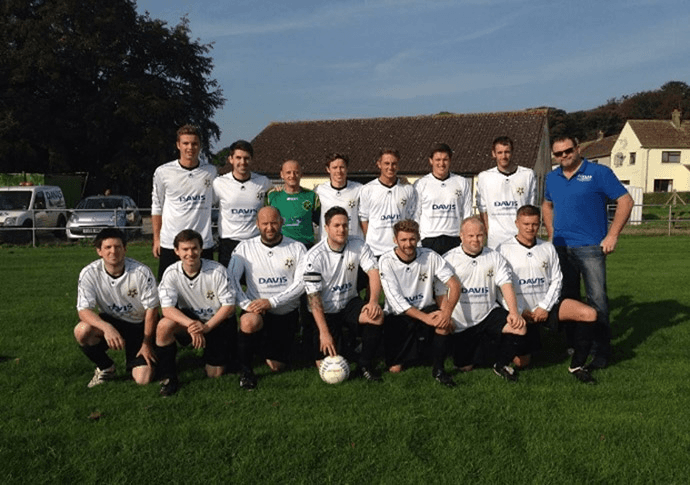 Soccer team in white jerseys with black shorts, posing outdoors on a green field.