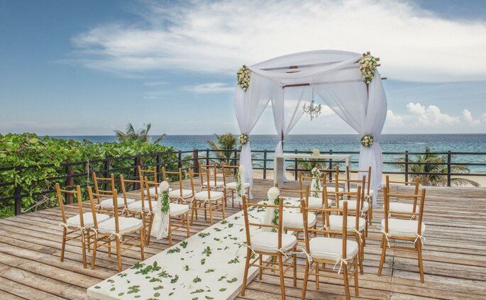 Se está celebrando una ceremonia de boda en una terraza de madera con vistas al océano.