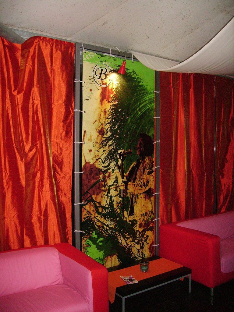 Interno con tende rosse, divani rosa, tavolo nero e opere d'arte colorate.