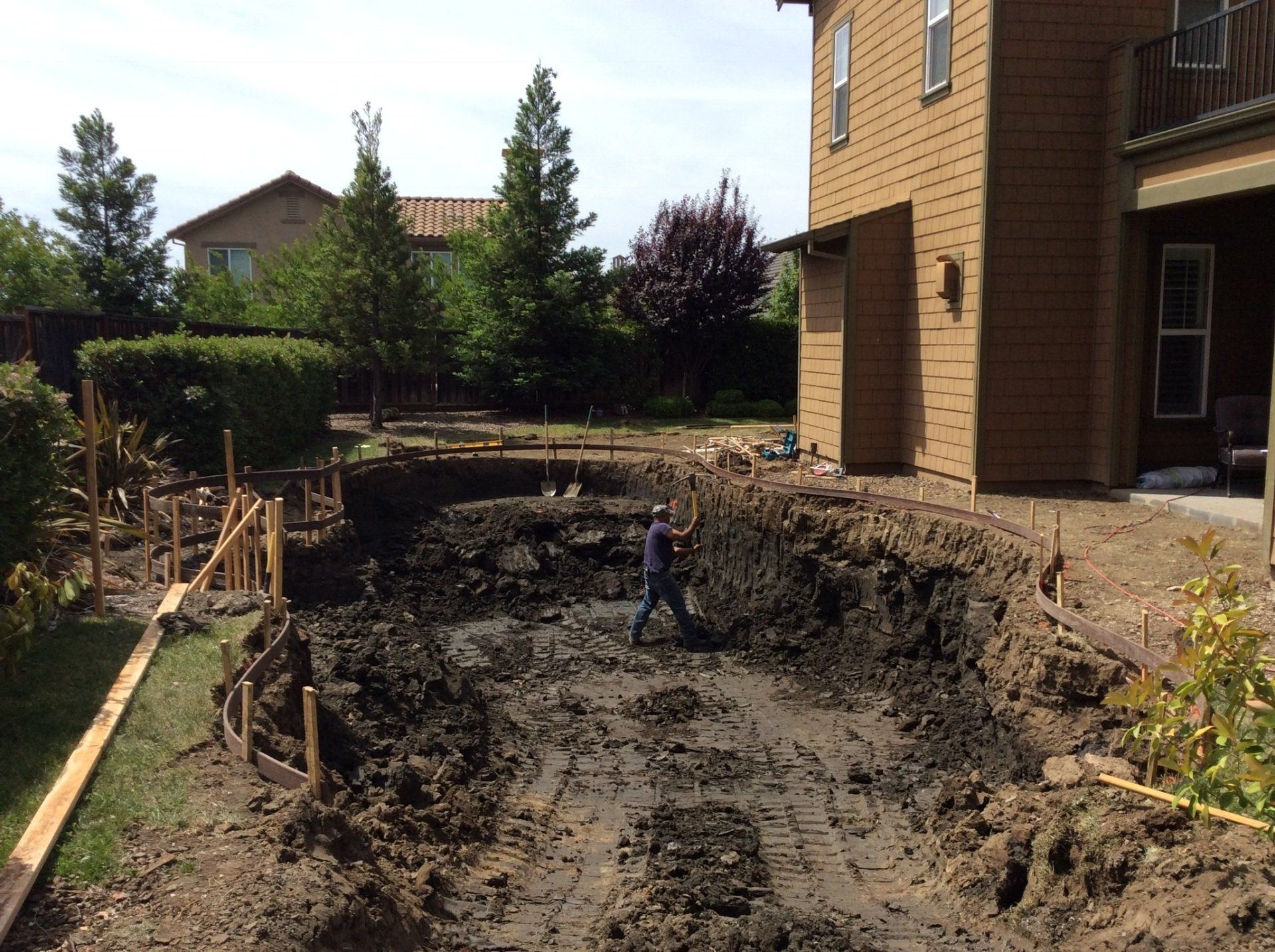 A man is digging a hole in the dirt in front of a house.