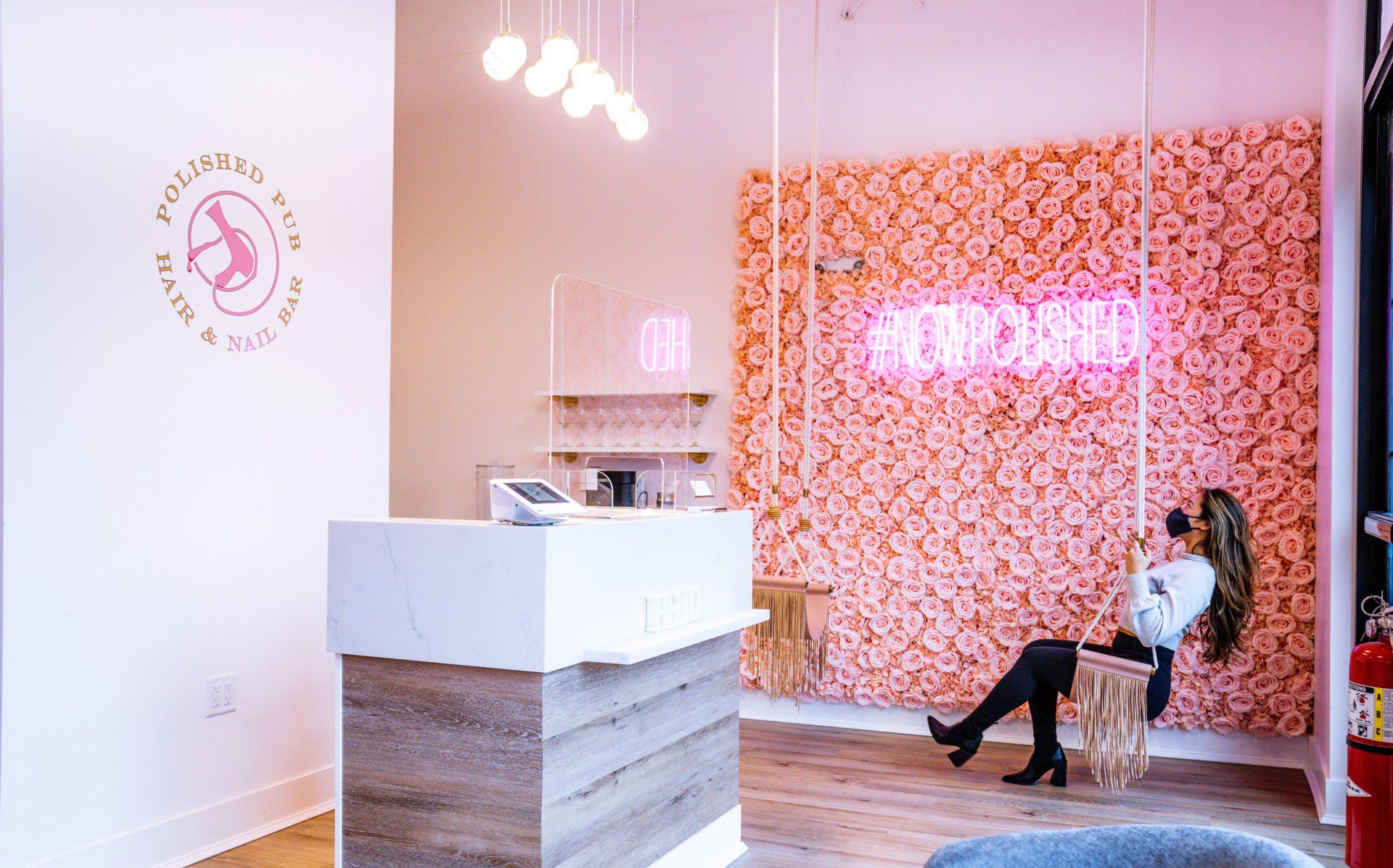 A woman is sitting in a chair in front of a pink wall.