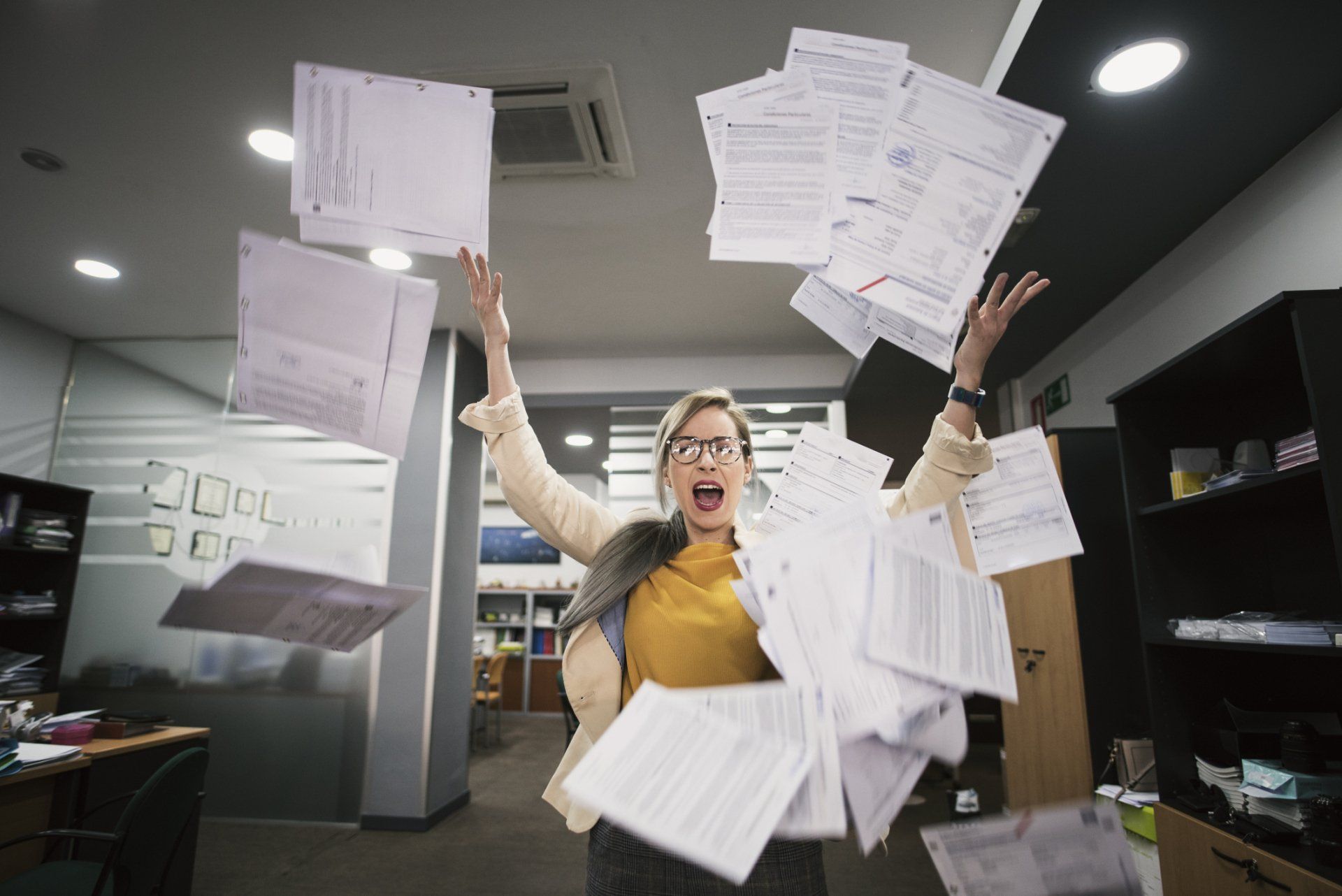 A woman is throwing papers in the air in an office.