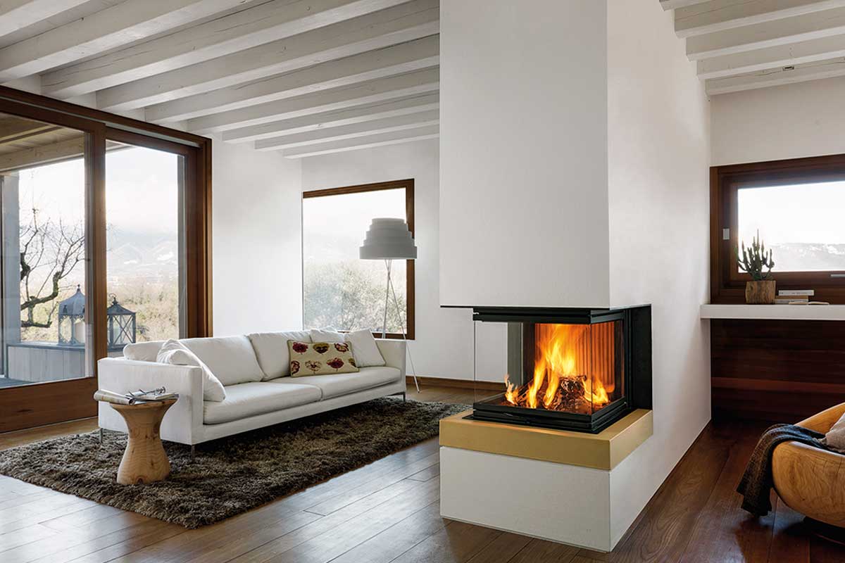 Soggiorno moderno con divano bianco, grande camino, tappeto scuro e dettagli in legno, con vista sul paesaggio innevato esterno.