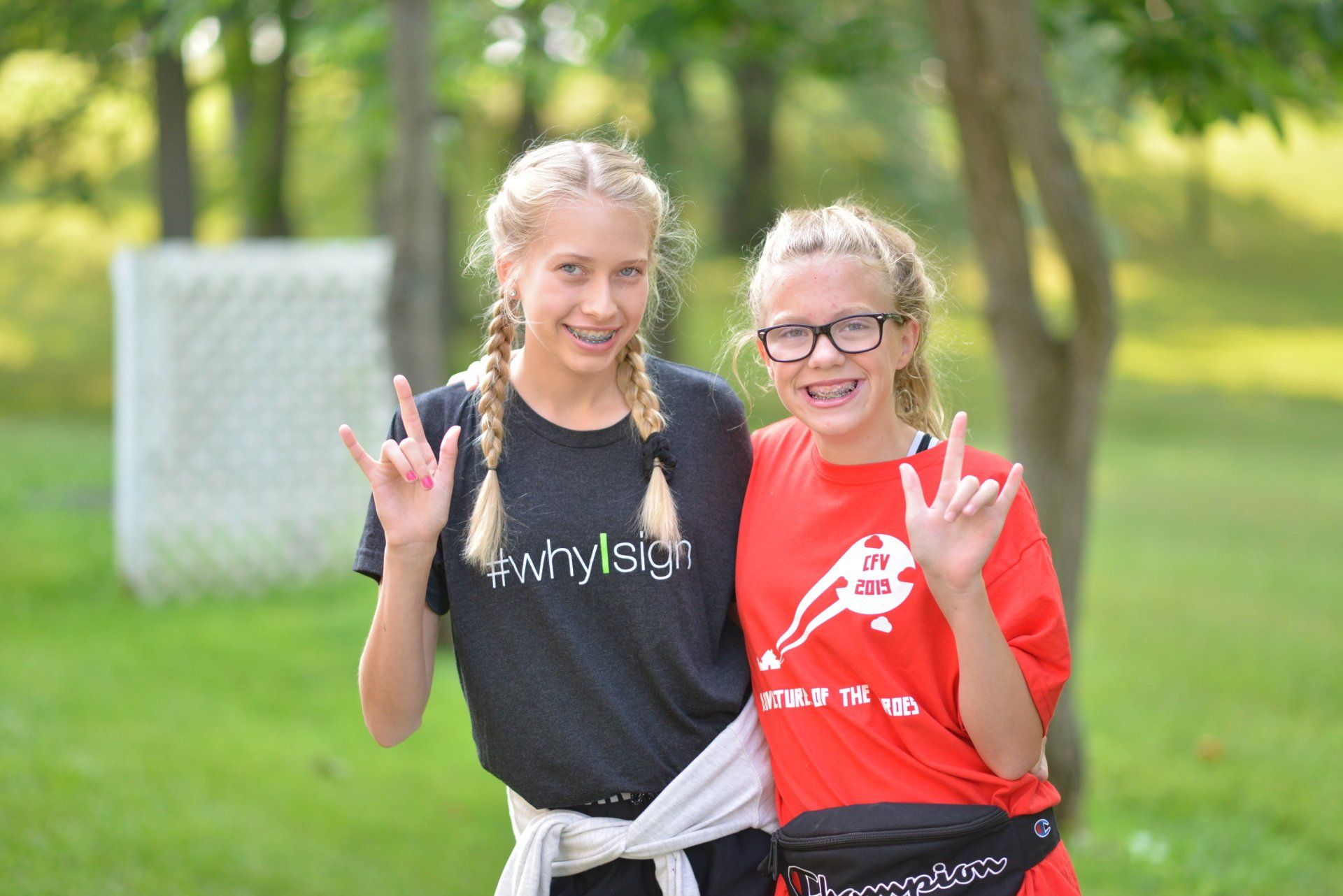 Two young girls are posing for a picture in a park.