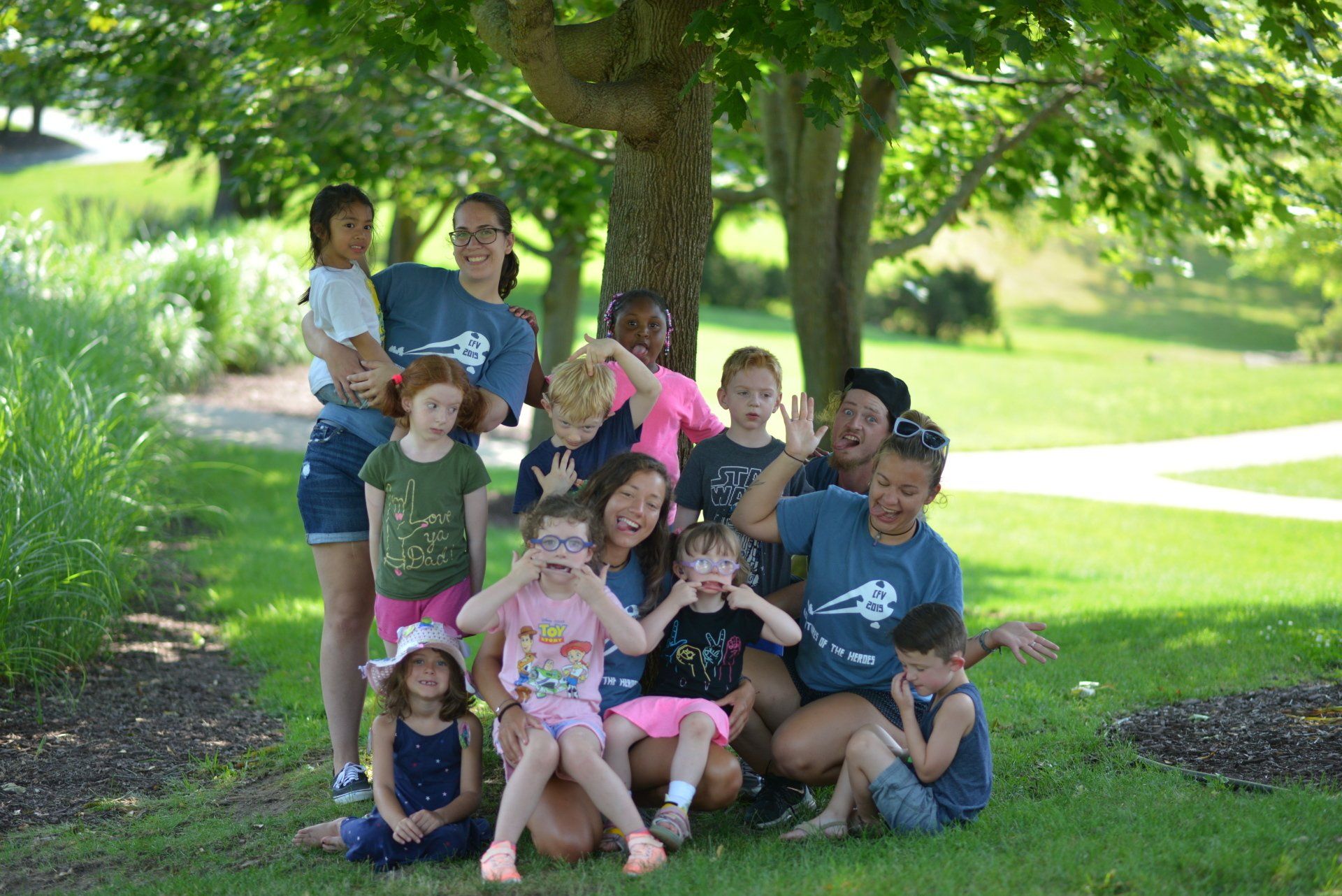 A group of children and adults are posing for a picture in a park.