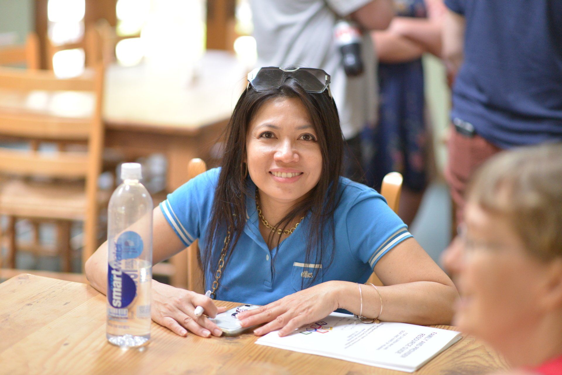A woman is sitting at a table with a bottle of smart water in front of her.
