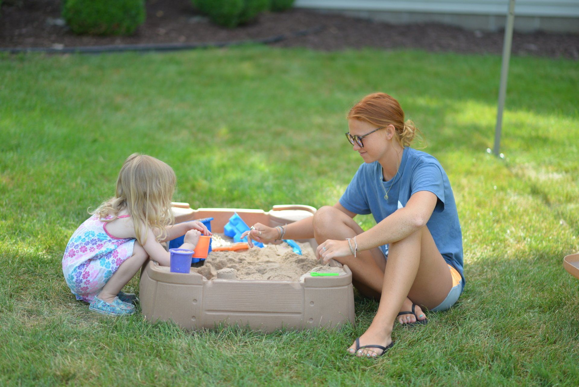 A woman and a little girl are playing in a sandbox.