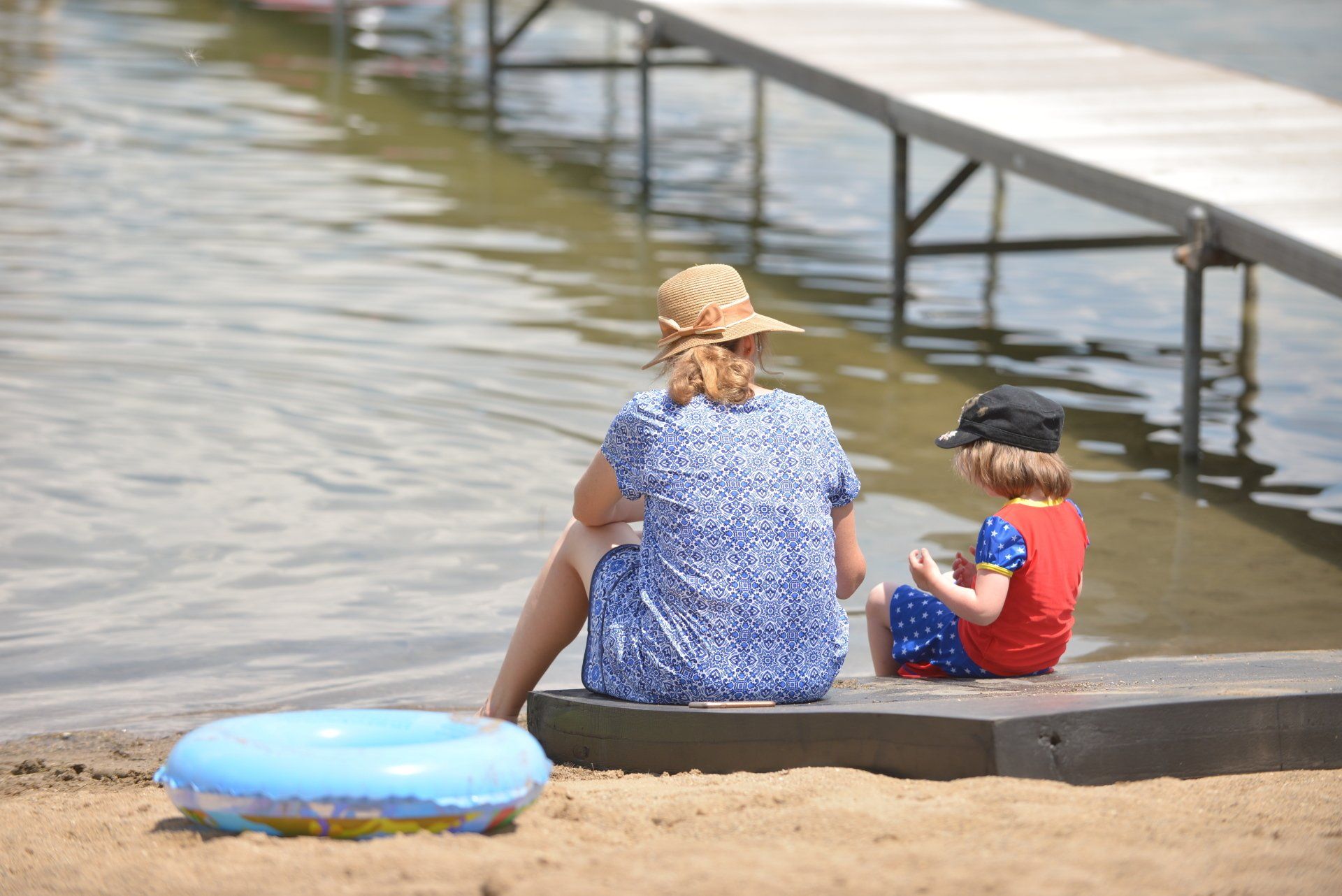 A woman and a child are sitting on a dock looking at the water.