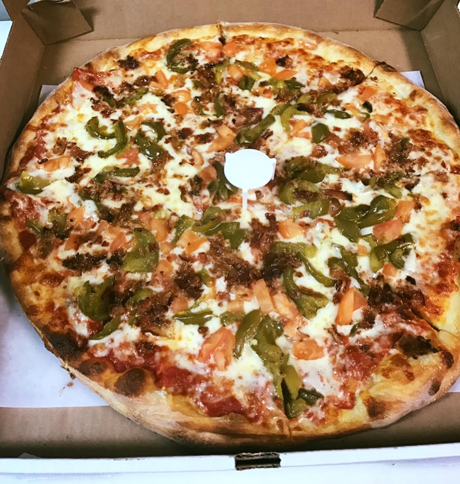 A pizza with tomatoes , peppers and cheese is in a cardboard box.