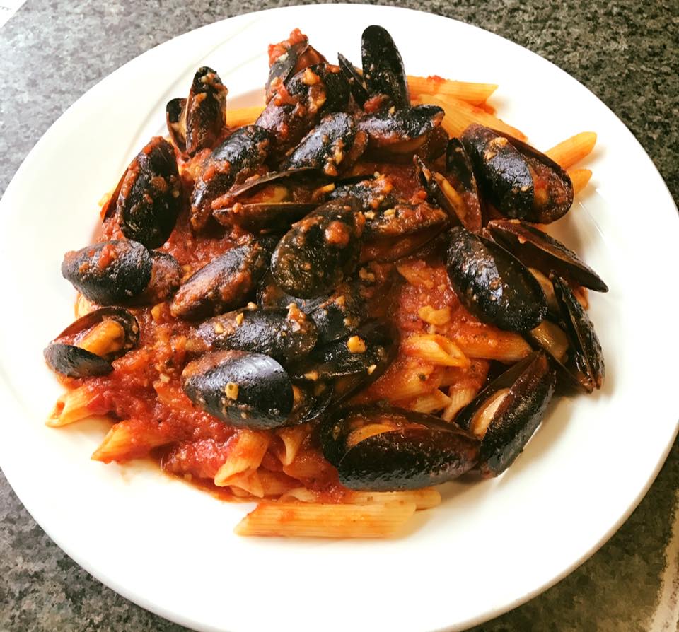 A white plate topped with pasta and mussels in a sauce
