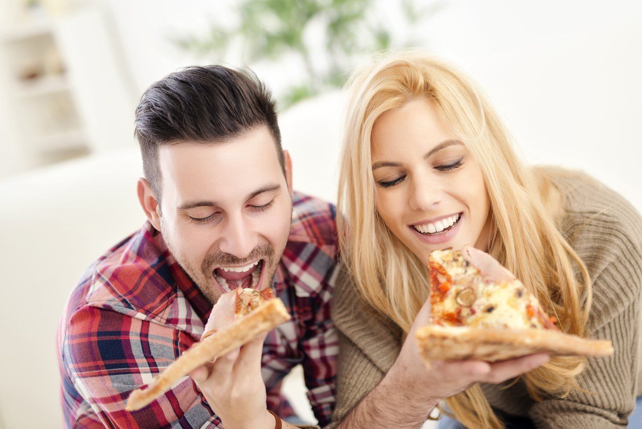 A man and a woman are eating slices of pizza together.