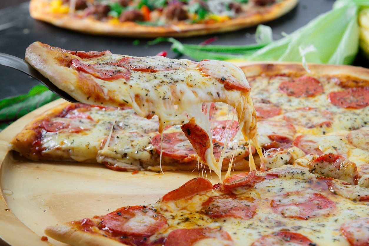 A slice of pepperoni pizza is being taken out of a pizza on a wooden plate.