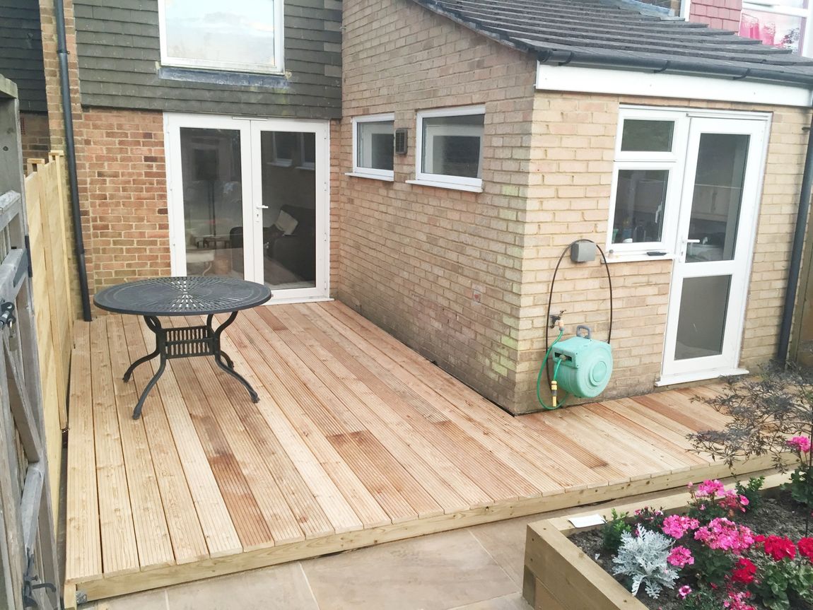 A wooden deck with a table in front of a brick house
