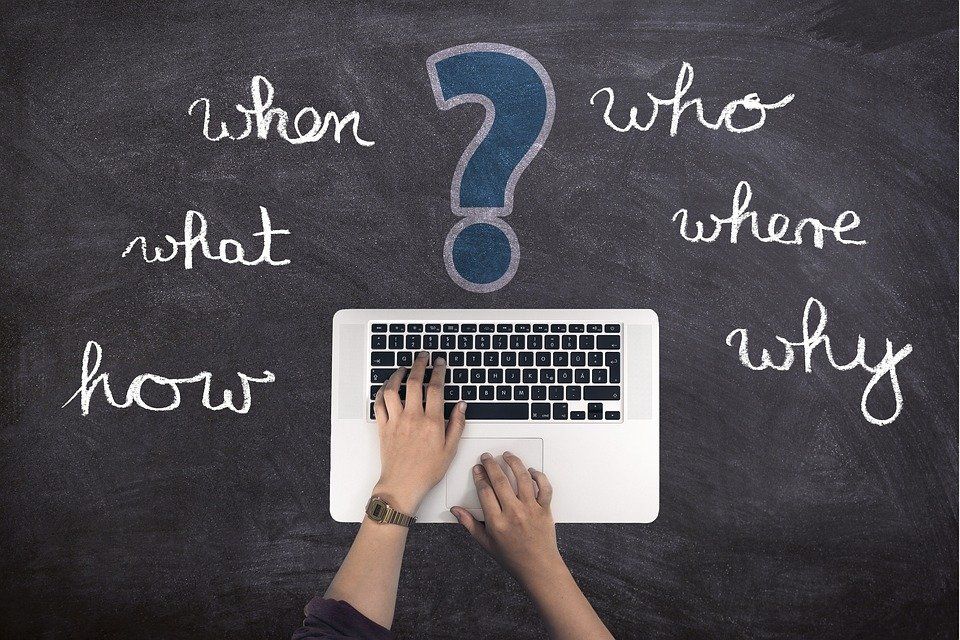 A person is typing on a laptop in front of a blackboard that says when what who where how and why