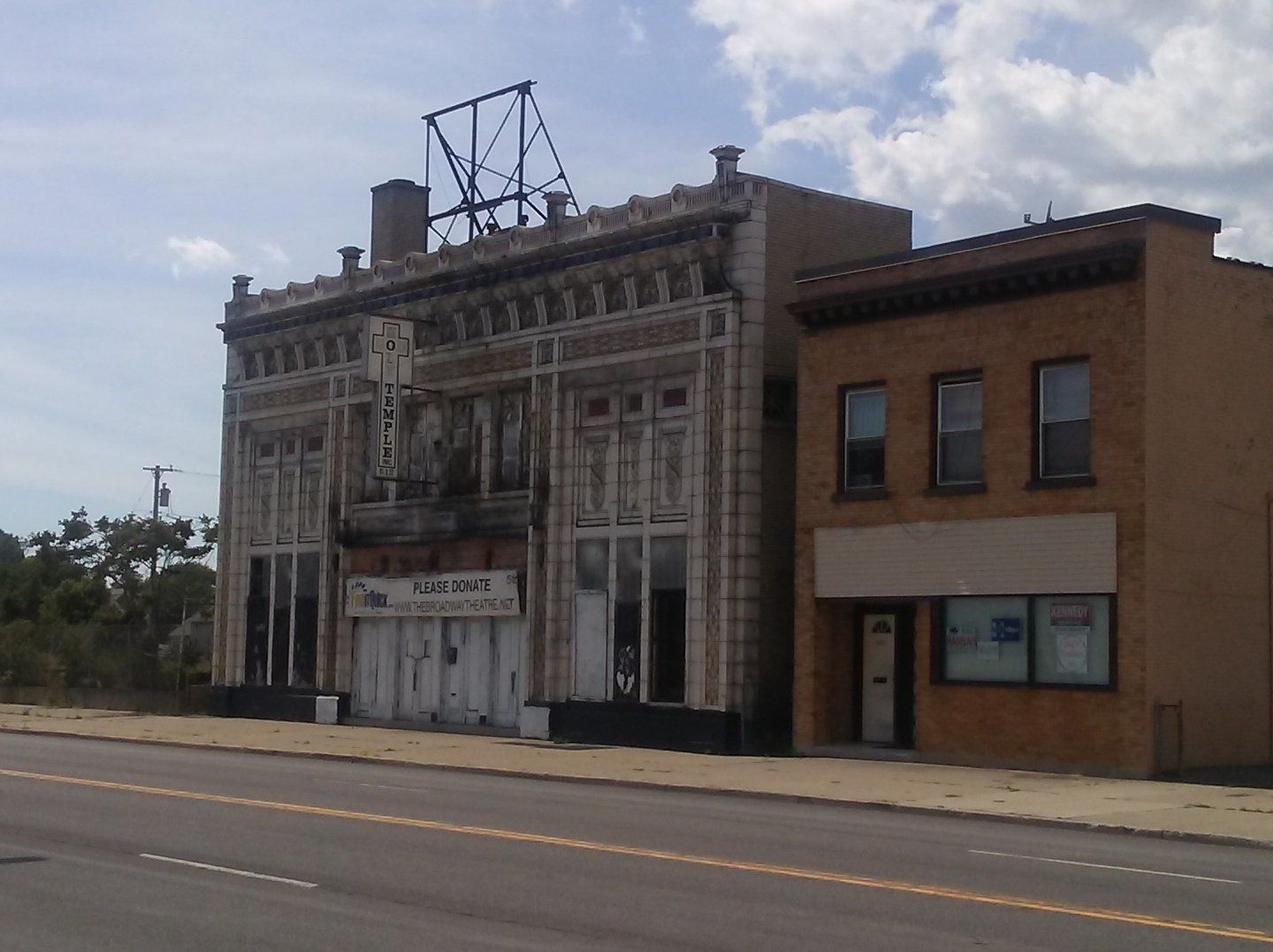 An old, ornate building next to a simple two-story brick building along a paved road under a cloudy sky.