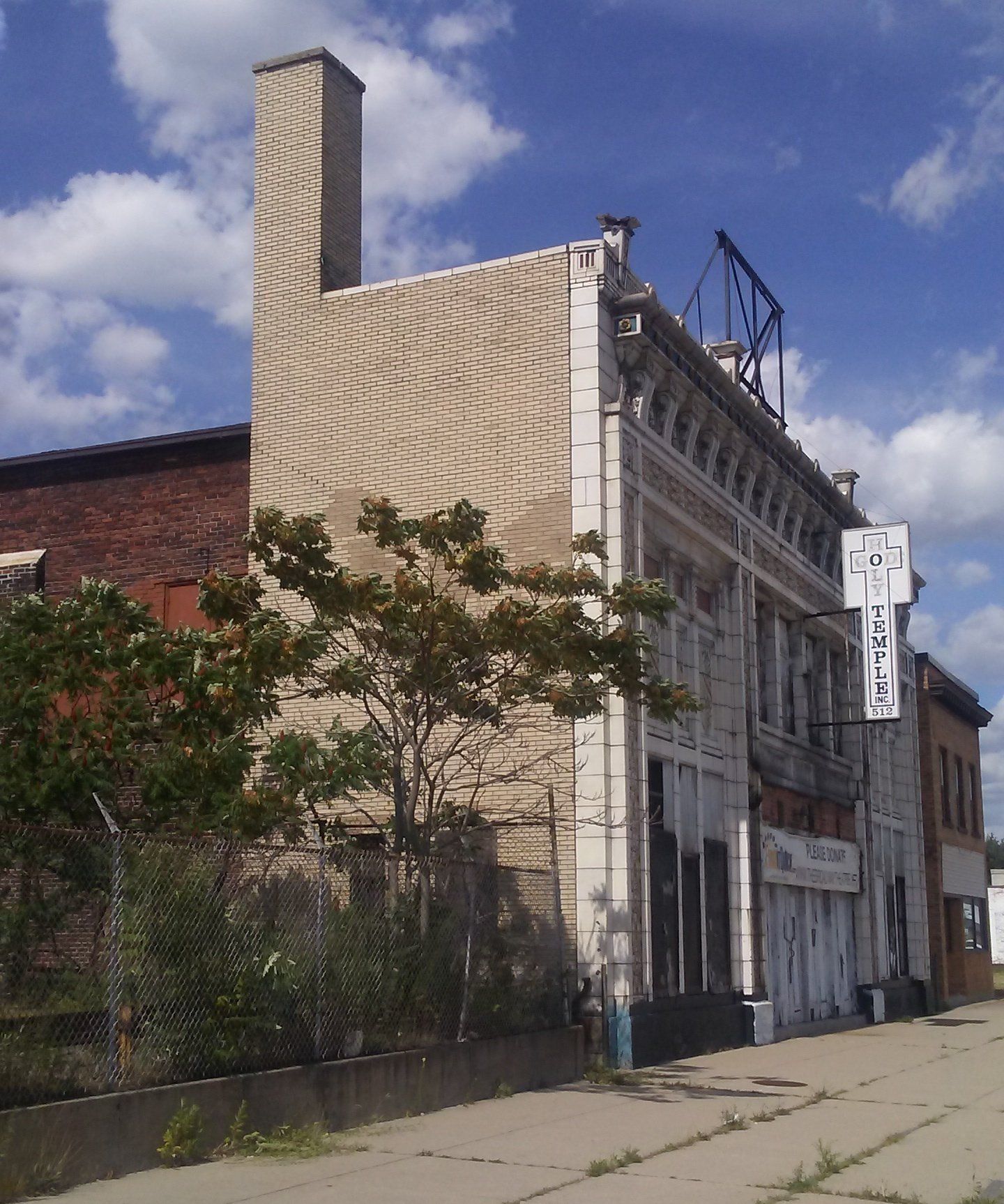 A weathered, multi-story brick building with a vertical sign and decorative facade stands along a cracked sidewalk.