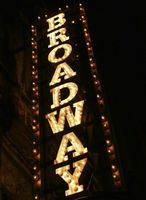 A vertical, illuminated Broadway sign featuring bright marquee lights against a dark background.