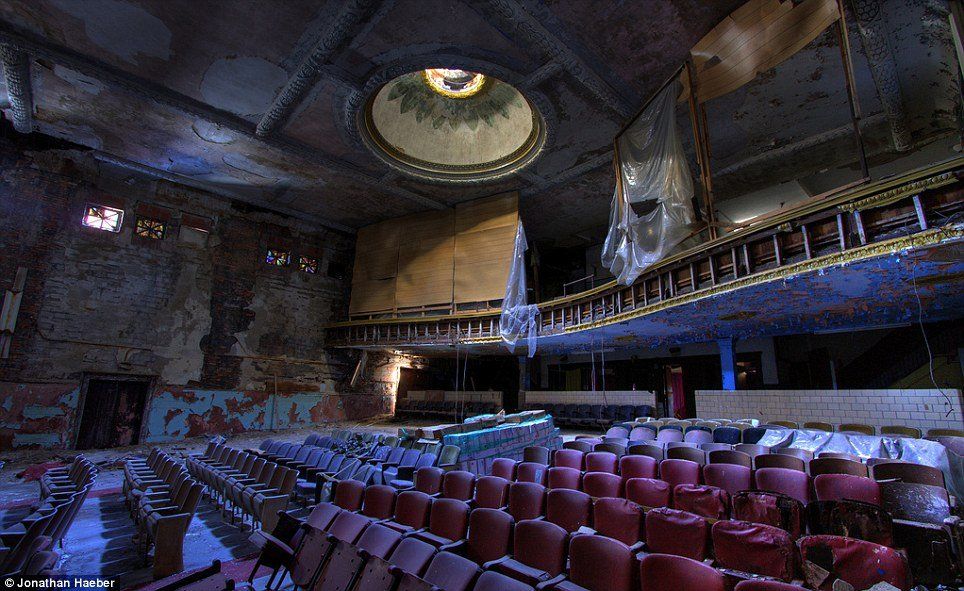 Abandoned theater with decaying red velvet seats, crumbling walls, and a domed ceiling under a dim, blue-lit atmosphere.