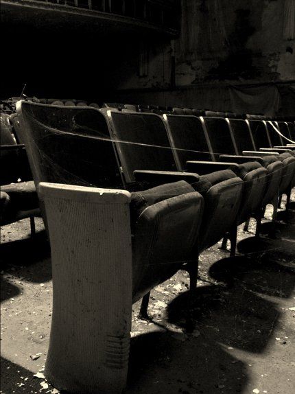 A row of dusty, worn theater seats in a dark, abandoned auditorium.