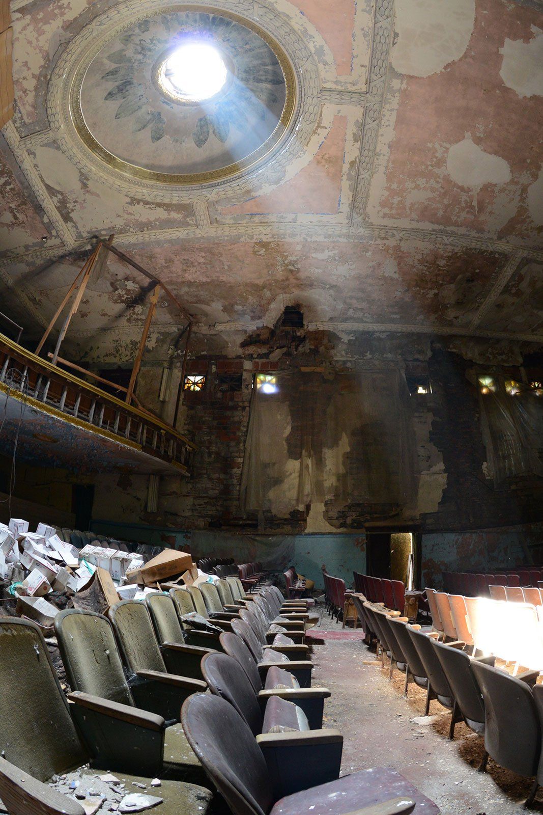 Abandoned theater with dusty rows of seats, peeling walls, and a sunlight-filled dome in the ceiling.