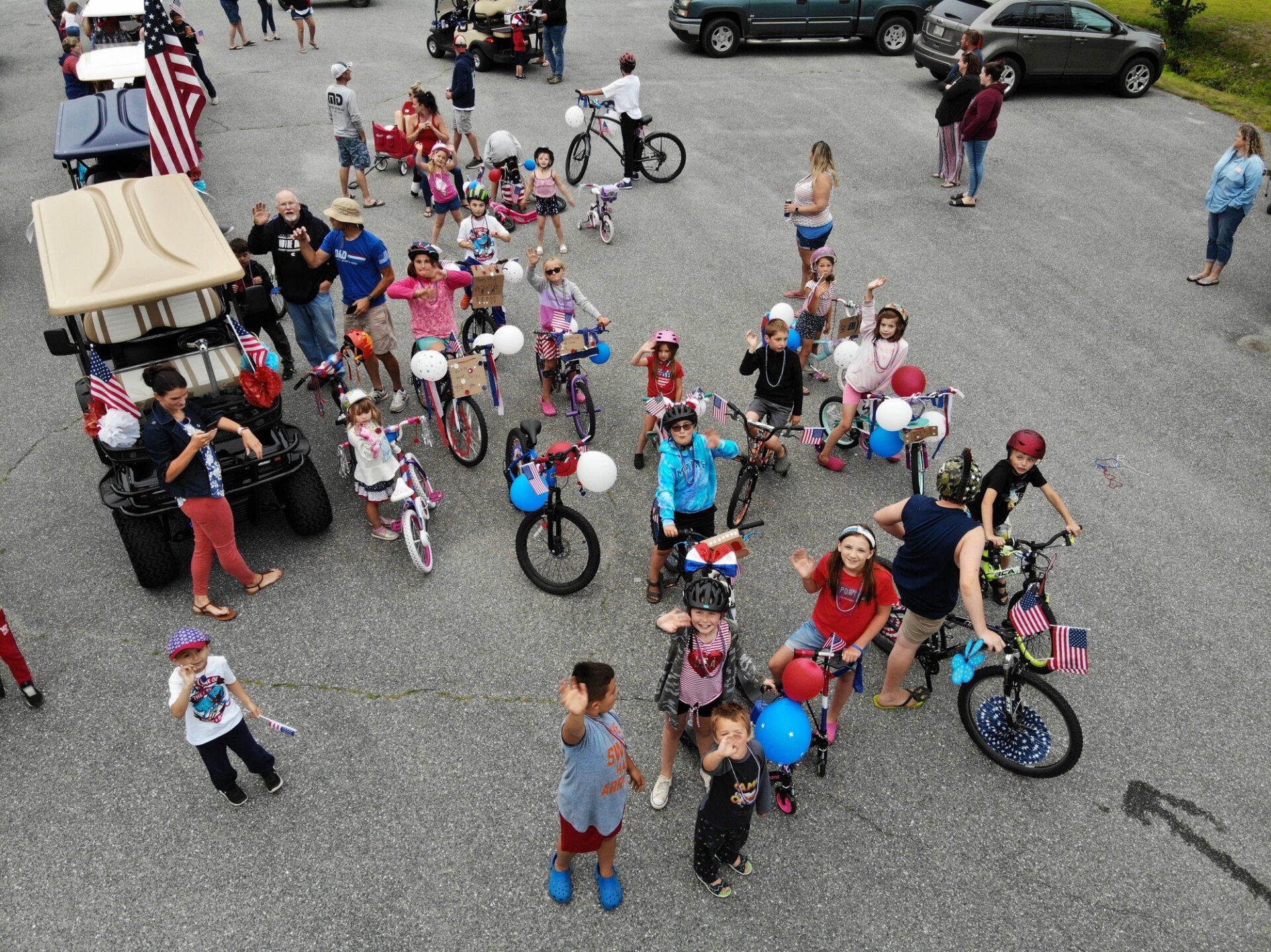 Group of cyclists with colorful balloons gathered in a parking lot, seen from above.