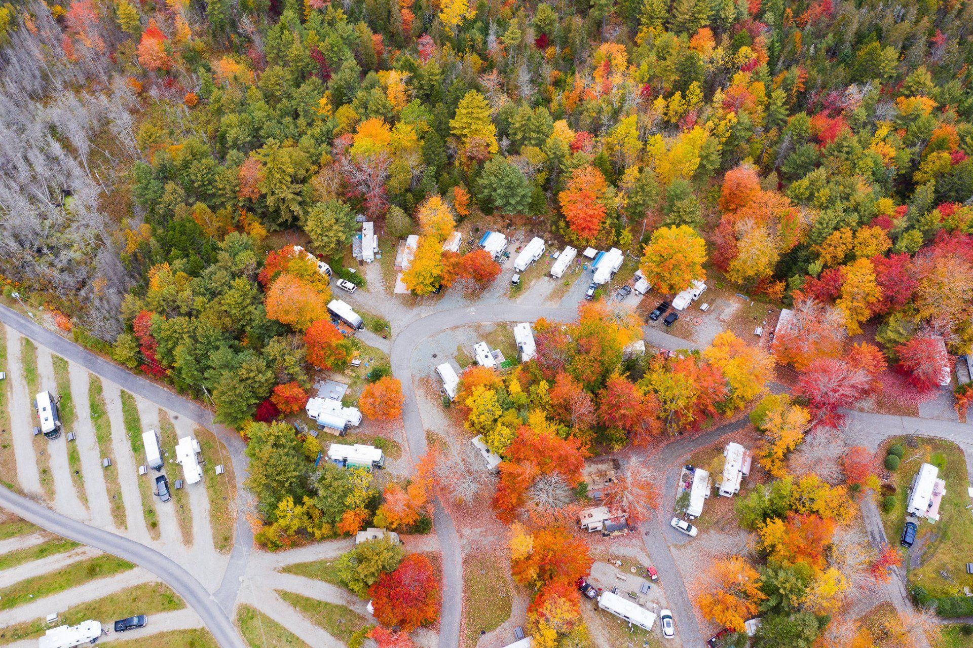 Aerial view of an autumn campground with RVs, tents, and winding roads surrounded by colorful trees