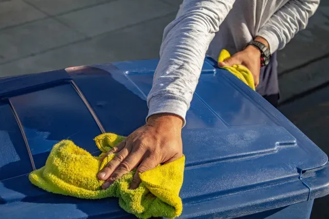 Person cleaning a blue plastic bin with a yellow cloth.
