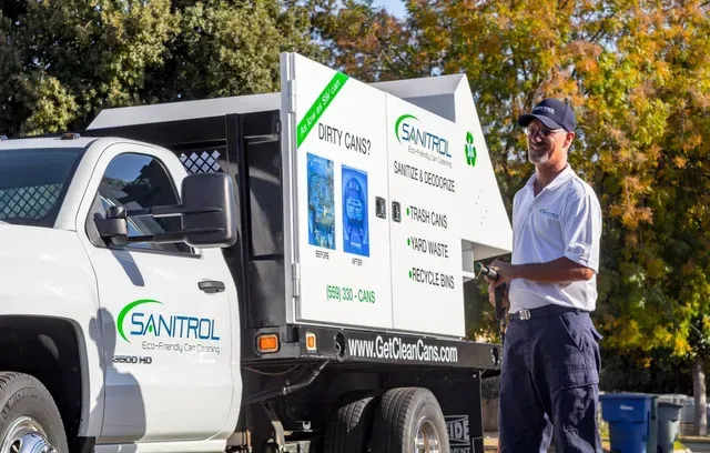 Man standing beside a white Santrol truck. Truck has a white container with labels. Sunny outdoor setting.