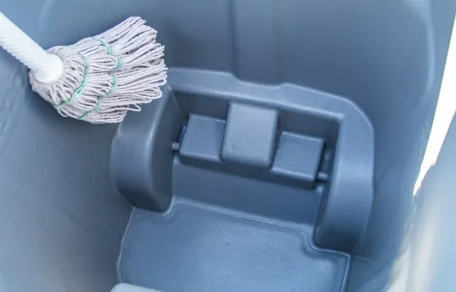 Inside a gray bucket, a white mop head rests on a built-in wringer.