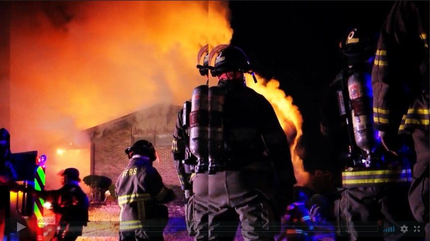 A team of firefighters work to quench a flaming building at night.