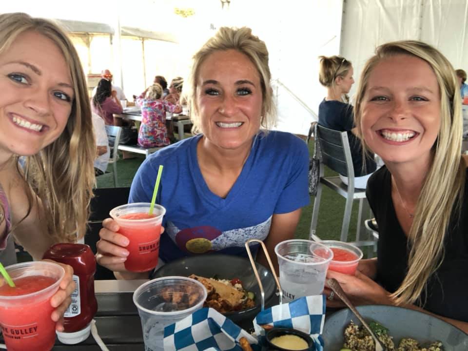 Three smiling people at an outdoor restaurant table with colorful drinks and food
