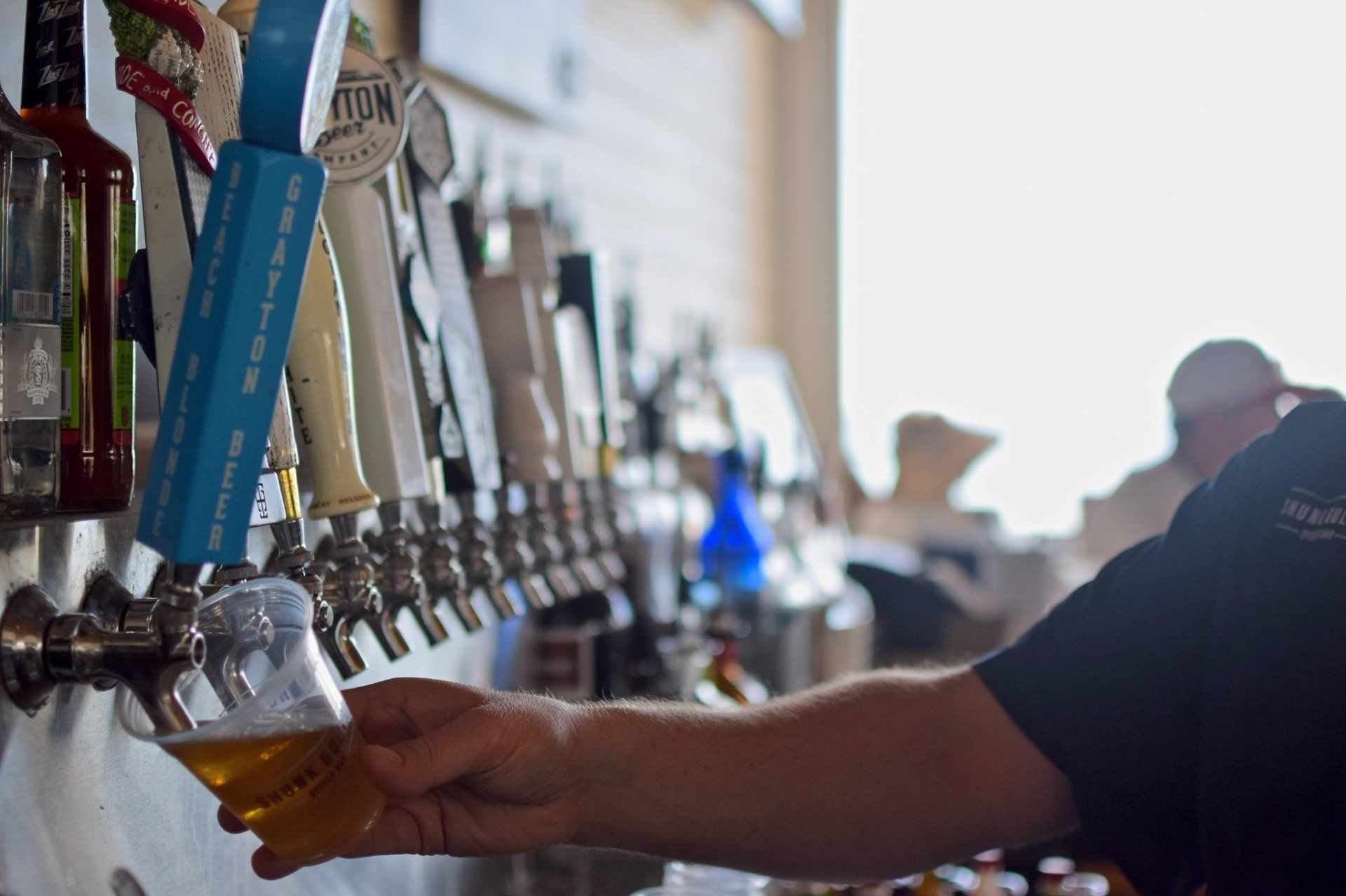 Person pouring beer from a tap in a bar with a row of metal taps