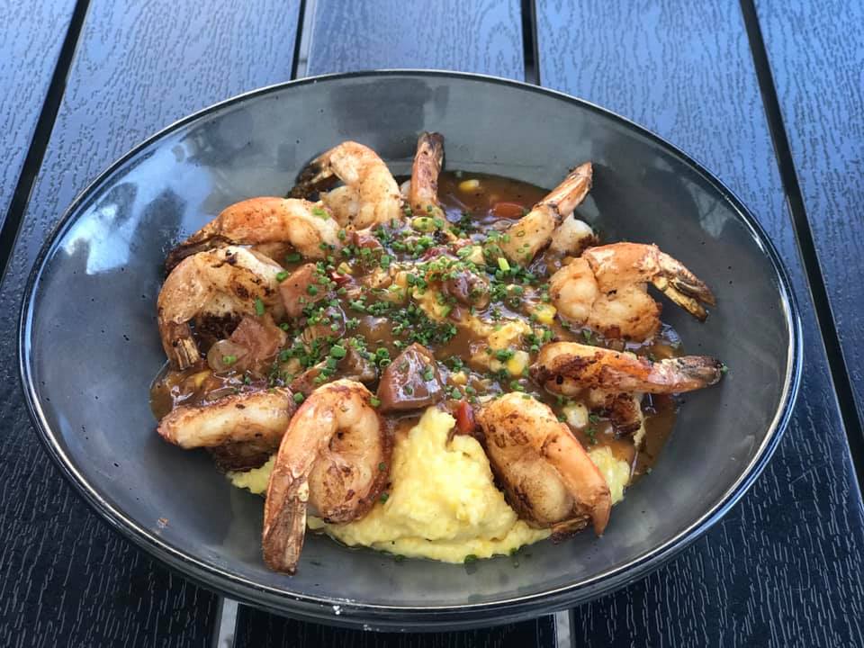 Plated shrimp over creamy mashed potatoes with herbs on a dark plate on a blue wooden table
