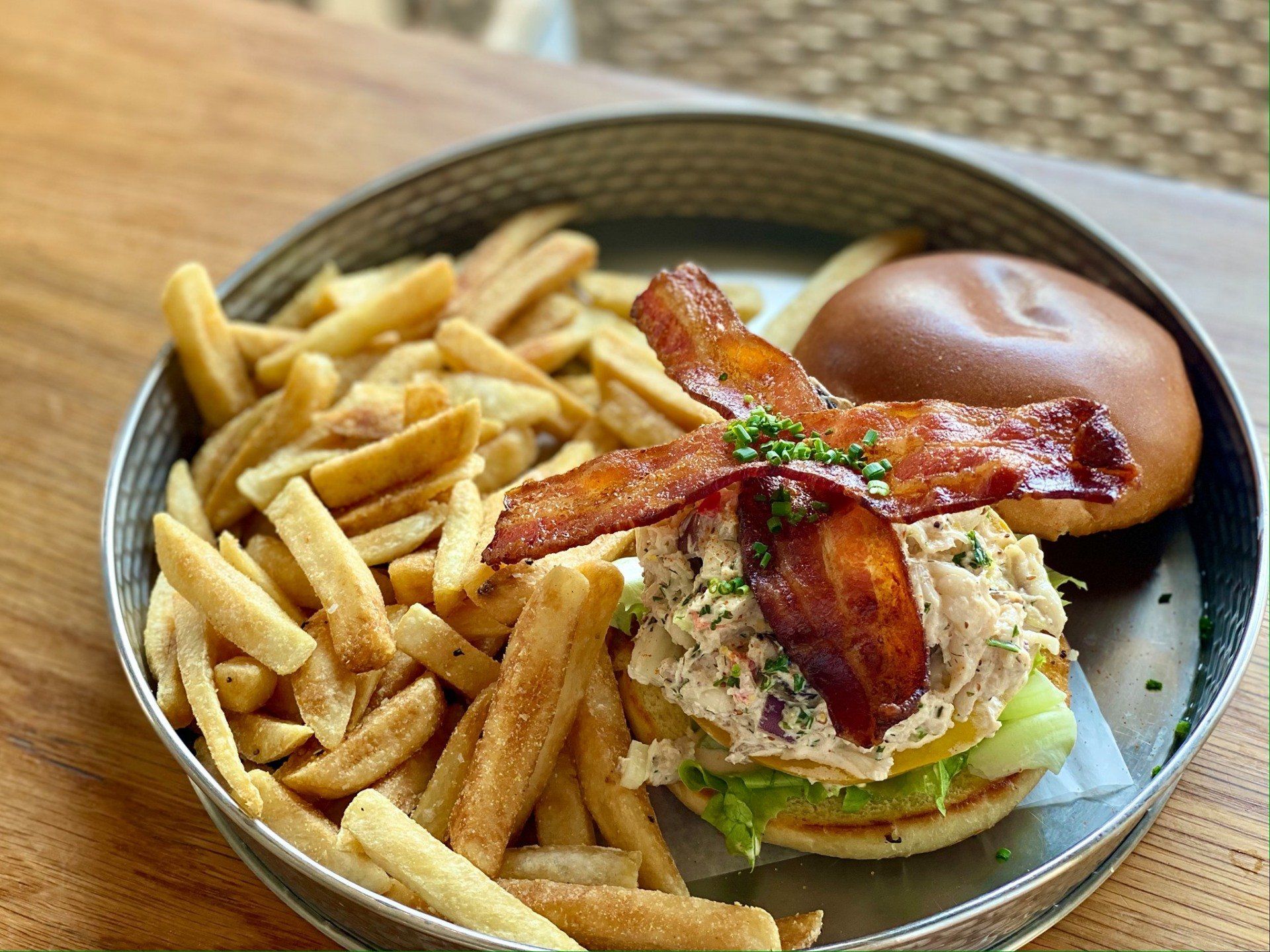 Plate with fries and a bacon-topped sandwich on a table