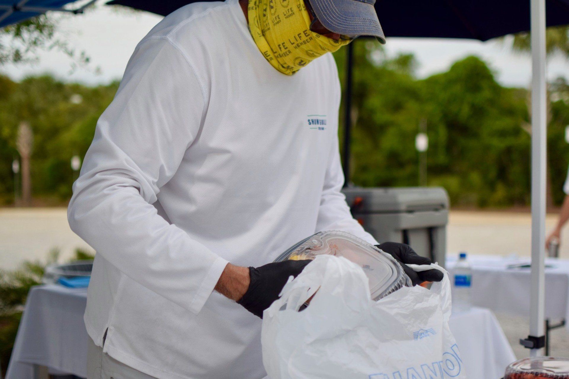 Person in white protective suit and face shield handling supplies at an outdoor table.