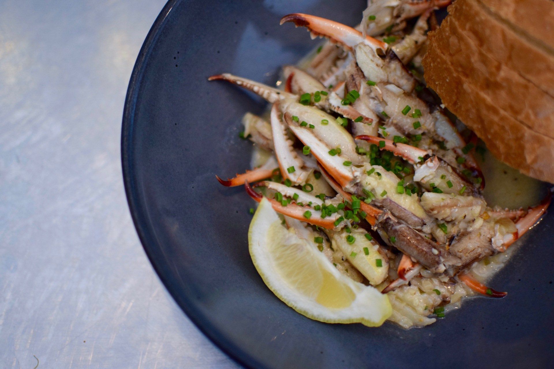 Plate of grilled crab legs with lemon wedges and herbs on a dark dish