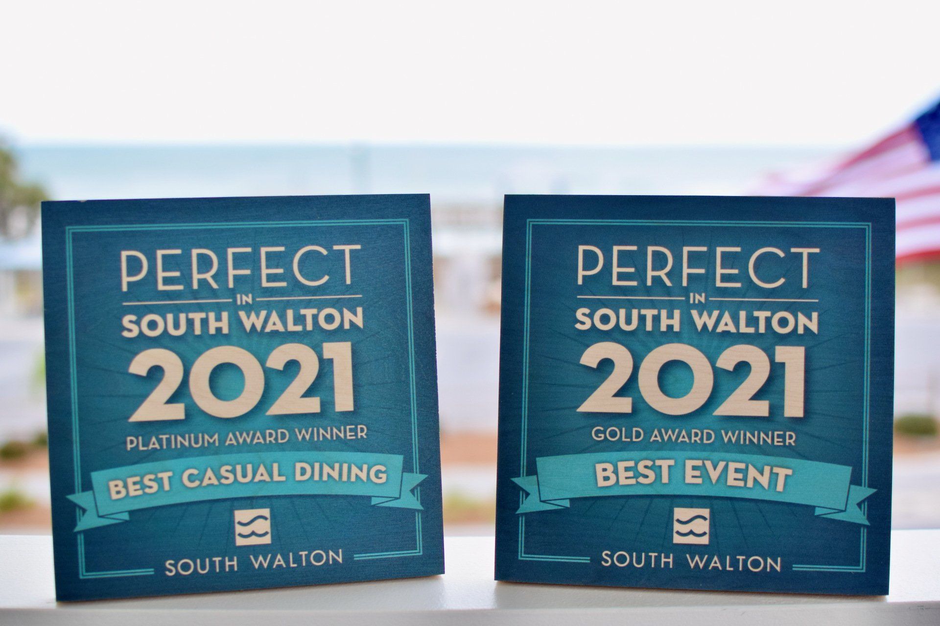 Two teal South Walton 2021 award plaques on a table, one for best casual dining and one for best event